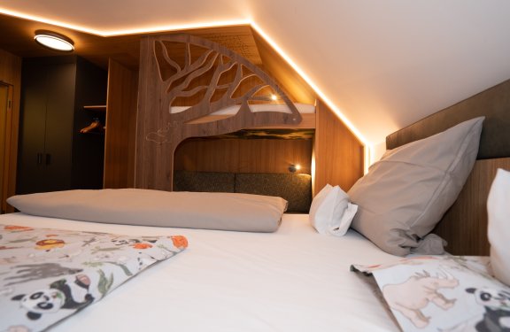 Blick über ein Bett mit Tierbettwäsche auf ein Etagenbett mit Baumdesign im Holzzimmer