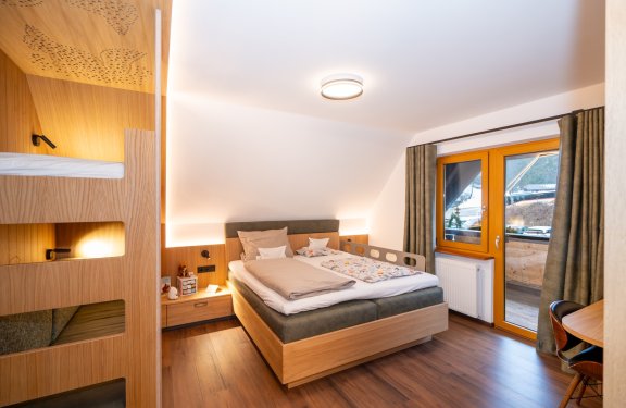 Gemütliches Schlafzimmer mit Doppelbett, Holzmöbeln, Fenster mit Vorhängen und Zugang zum Balkon