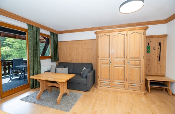 Wohnzimmer mit Holzmöbeln, grauem Sofa, Tisch und Balkon mit grünen Vorhängen
