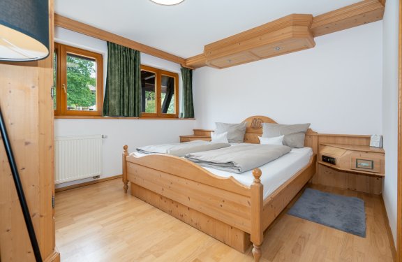 Hell eingerichtetes Schlafzimmer mit Holzmöbeln, Doppelbett und grünen Vorhängen am Fenster